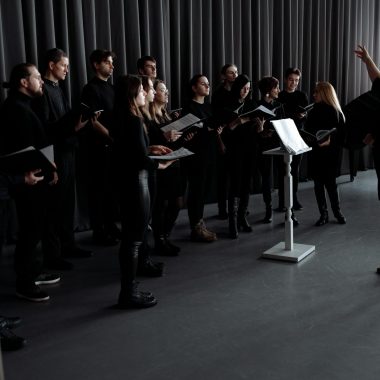 A choir practicing under a conductor's guidance in an indoor studio setting.