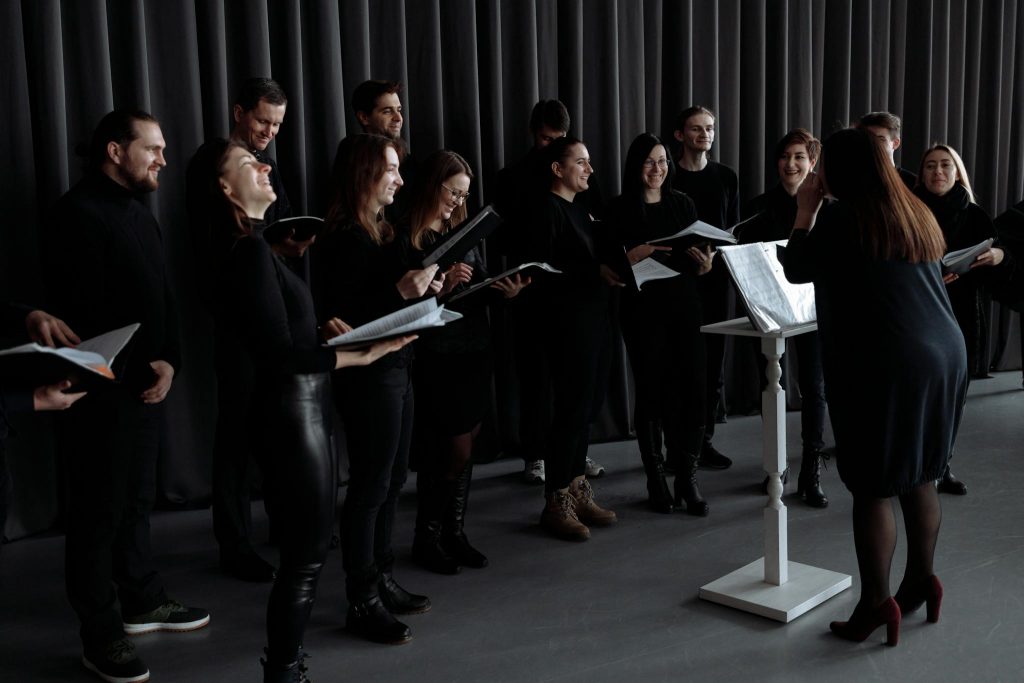 A group of men and women singing with a conductor during choir practice.