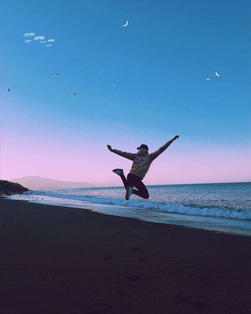 A man jumping on a beach under a crescent moon, symbolizing freedom and joy.